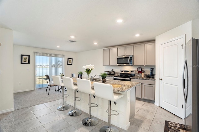 kitchen featuring light stone counters, stainless steel appliances, a breakfast bar, a kitchen island with sink, and gray cabinetry