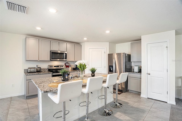 kitchen featuring stainless steel appliances, a center island with sink, and gray cabinets