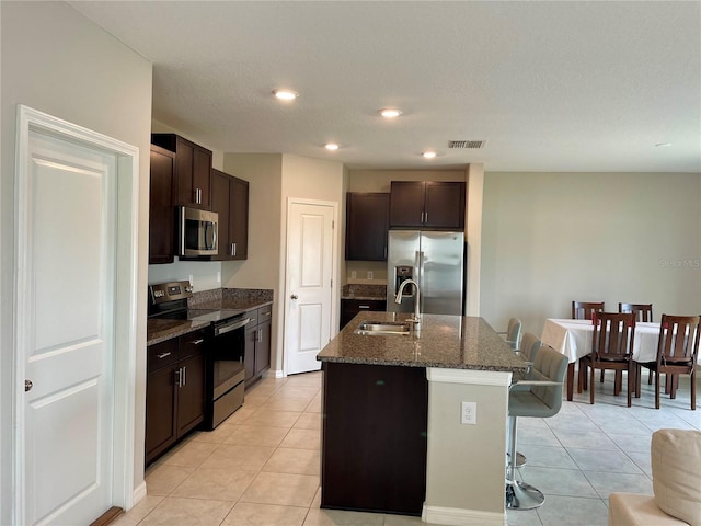 kitchen with appliances with stainless steel finishes, a breakfast bar, sink, light tile patterned floors, and a center island with sink