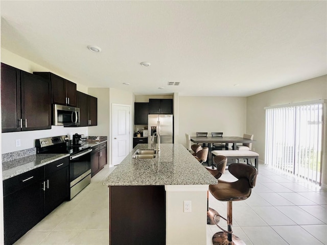 kitchen featuring sink, appliances with stainless steel finishes, a kitchen breakfast bar, light stone countertops, and a center island with sink