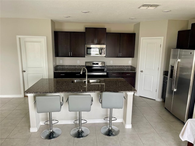 kitchen with light tile patterned flooring, a kitchen bar, sink, an island with sink, and stainless steel appliances