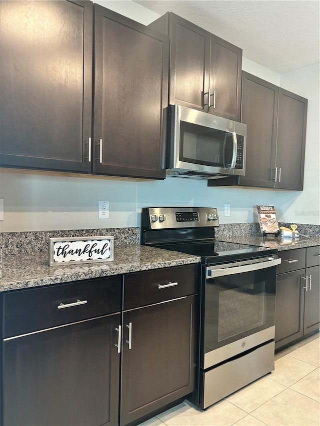 kitchen with stone counters, appliances with stainless steel finishes, dark brown cabinets, and light tile patterned floors