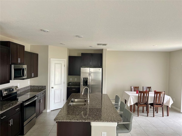 13621 Willow Bluestar Loop, Riverview, FL 33579 - kitchen with appliances with stainless steel finishes, light tile patterned floors, a center island with sink, dark stone countertops, and a textured ceiling