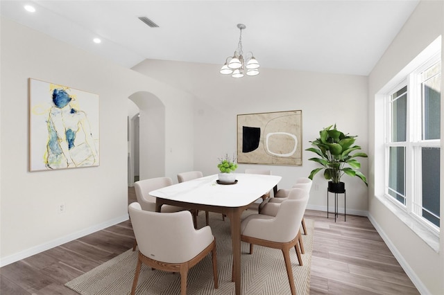 dining space with hardwood / wood-style floors, a healthy amount of sunlight, vaulted ceiling, and a notable chandelier