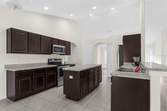 kitchen with sink, stainless steel appliances, lofted ceiling, a kitchen island with sink, and light tile patterned flooring