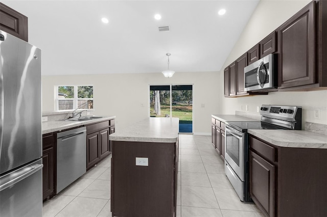 kitchen with light tile patterned flooring, vaulted ceiling, appliances with stainless steel finishes, decorative light fixtures, and a kitchen island