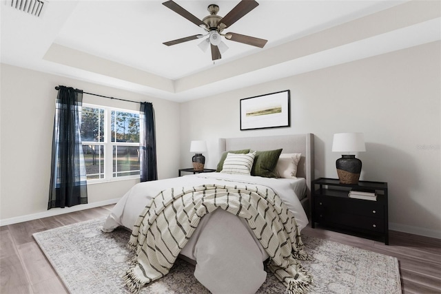 bedroom with hardwood / wood-style floors, ceiling fan, and a raised ceiling