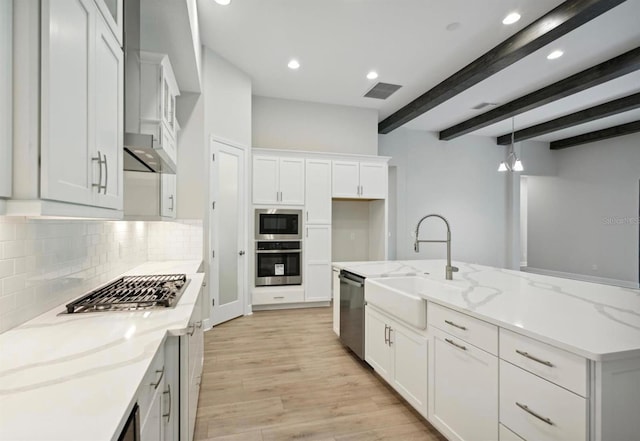 kitchen featuring white cabinets, stainless steel appliances, light stone counters, and beam ceiling