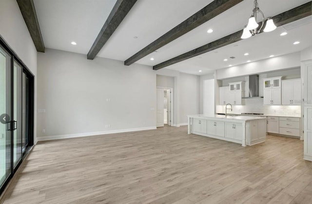 kitchen featuring pendant lighting, wall chimney exhaust hood, backsplash, a kitchen island with sink, and light hardwood / wood-style floors