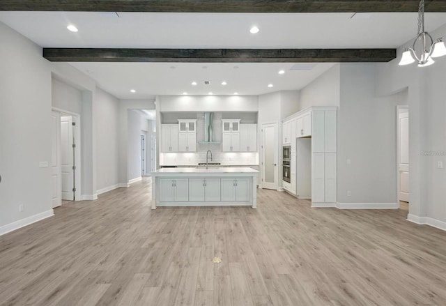 kitchen featuring white cabinetry, sink, light hardwood / wood-style flooring, a center island with sink, and wall chimney exhaust hood