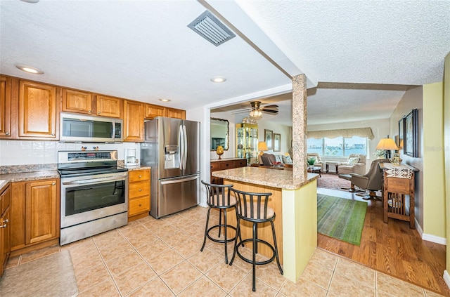 kitchen with ceiling fan, light tile patterned floors, a breakfast bar area, a kitchen island, and appliances with stainless steel finishes