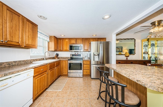 kitchen with a kitchen breakfast bar, stainless steel appliances, ceiling fan, sink, and light tile patterned floors