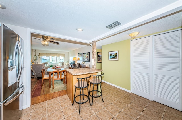 kitchen with a textured ceiling, ceiling fan, stainless steel refrigerator with ice dispenser, and tile patterned floors