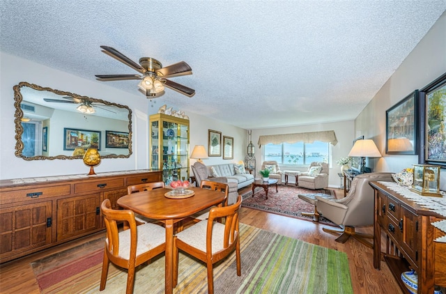 dining area with ceiling fan, wood-type flooring, and a textured ceiling