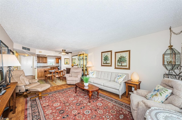 living room with ceiling fan, wood-type flooring, and a textured ceiling