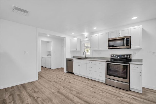 kitchen with sink, appliances with stainless steel finishes, washing machine and clothes dryer, white cabinets, and light wood-type flooring