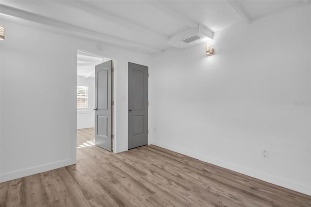 unfurnished room with beamed ceiling and light wood-type flooring