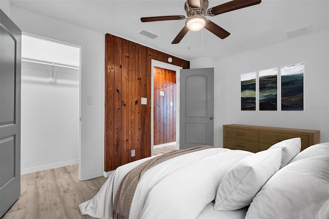 bedroom featuring ceiling fan, wooden walls, a walk in closet, a closet, and light wood-type flooring