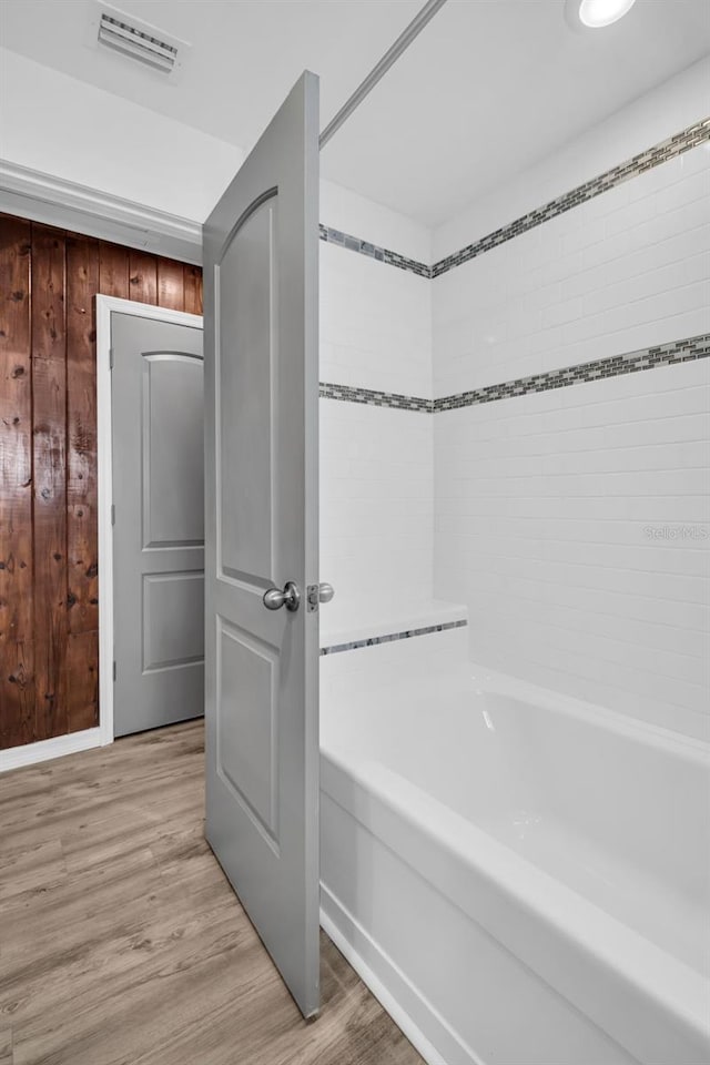 bathroom with hardwood / wood-style floors, a bathtub, and wooden walls