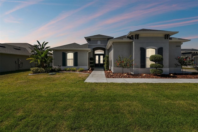 view of front of property featuring stucco siding, french doors, and a yard