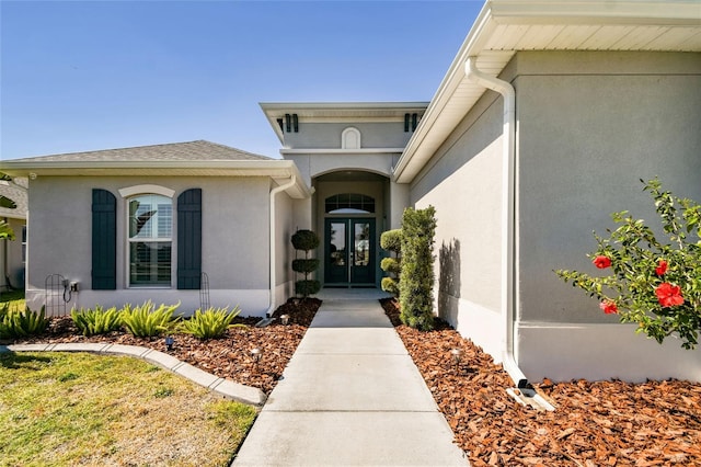 view of exterior entry featuring a shingled roof, french doors, and stucco siding