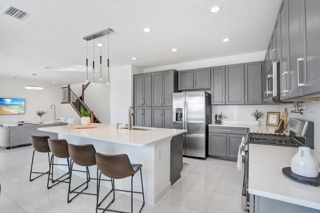 kitchen featuring appliances with stainless steel finishes, sink, light tile patterned floors, pendant lighting, and a center island with sink