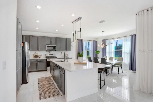 kitchen with a kitchen island with sink, sink, appliances with stainless steel finishes, decorative light fixtures, and light tile patterned flooring