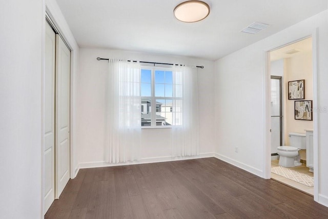 unfurnished bedroom featuring ensuite bathroom, a closet, and dark hardwood / wood-style floors