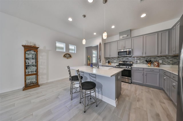 kitchen with sink, an island with sink, pendant lighting, gray cabinets, and appliances with stainless steel finishes