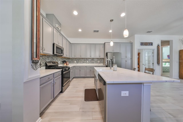 kitchen featuring a kitchen island with sink, pendant lighting, a kitchen bar, decorative backsplash, and appliances with stainless steel finishes