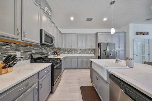 kitchen with sink, hanging light fixtures, tasteful backsplash, light stone counters, and appliances with stainless steel finishes