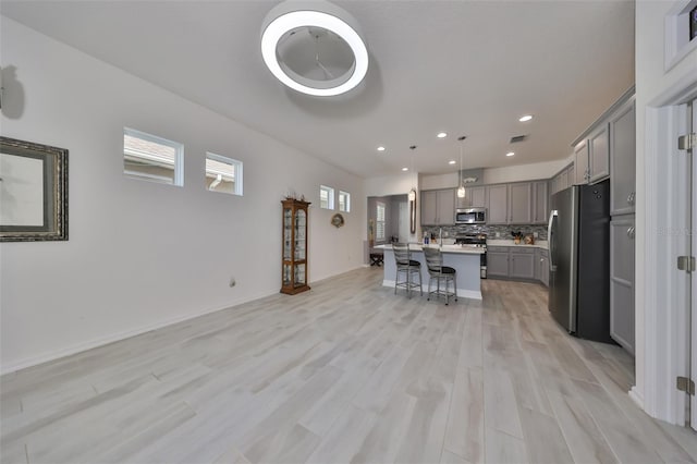 kitchen featuring gray cabinetry, a breakfast bar, stainless steel appliances, a kitchen island with sink, and decorative light fixtures