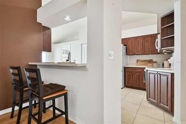 kitchen with lofted ceiling, a kitchen bar, kitchen peninsula, light tile patterned flooring, and stainless steel refrigerator