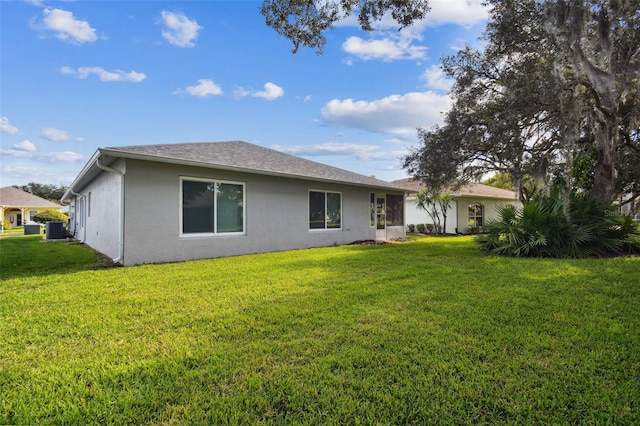 rear view of property with central AC unit and a yard