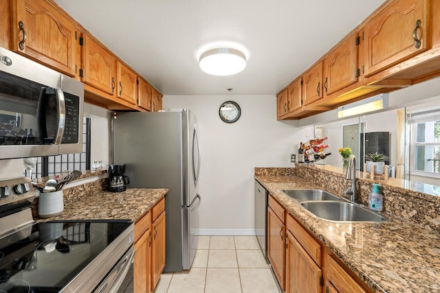 kitchen featuring light tile patterned flooring, appliances with stainless steel finishes, dark stone countertops, and sink