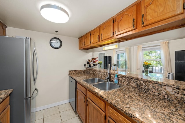 kitchen with dark stone counters, sink, light tile patterned flooring, and stainless steel appliances