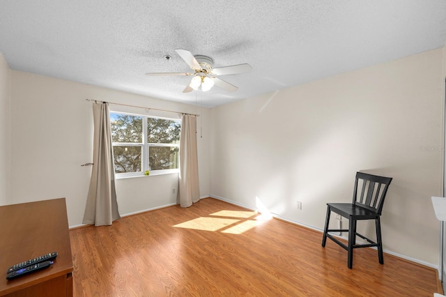 living area with ceiling fan, light wood-type flooring, and a textured ceiling