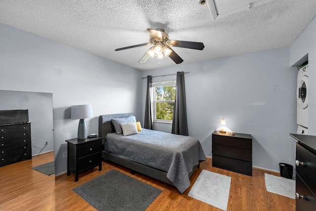 bedroom with a textured ceiling, ceiling fan, wood-type flooring, and stacked washer and dryer