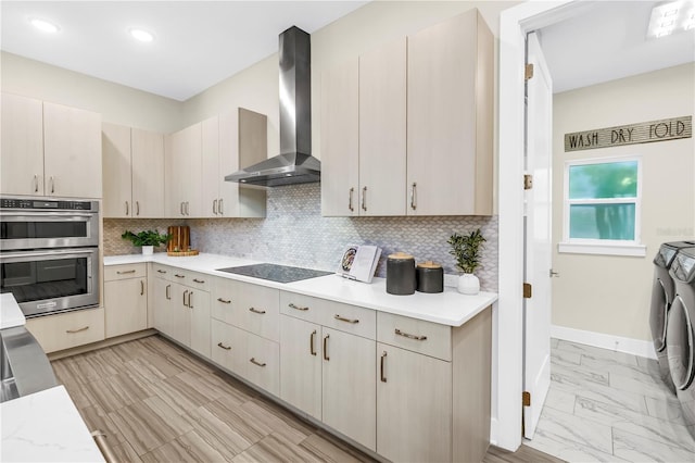 2246 Fiesta Dr, Sarasota, FL 34231 - kitchen featuring washer and dryer, wall chimney exhaust hood, double oven, black electric cooktop, and light countertops