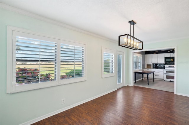 unfurnished living room with crown molding, dark wood-type flooring, and an inviting chandelier