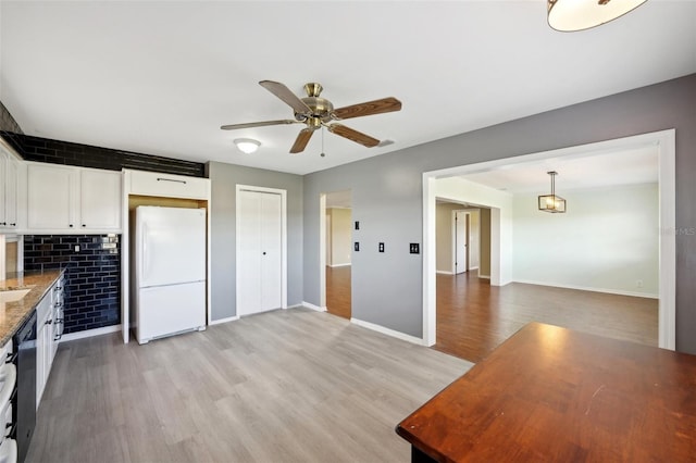 kitchen with light stone countertops, light wood-type flooring, white fridge, white cabinetry, and hanging light fixtures