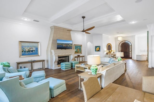 living room with ceiling fan, dark wood-type flooring, beamed ceiling, a fireplace, and ornamental molding