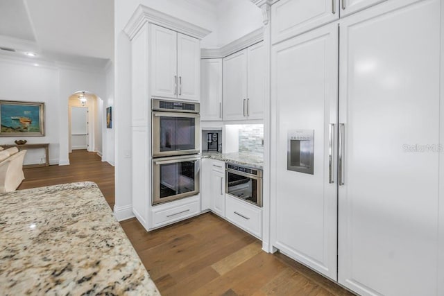 kitchen featuring white cabinets, light stone counters, double oven, tasteful backsplash, and dark hardwood / wood-style flooring