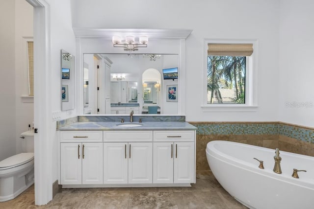 bathroom featuring a washtub, vanity, a notable chandelier, and toilet