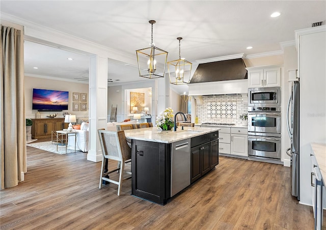 kitchen featuring a center island with sink, a breakfast bar, white cabinetry, and appliances with stainless steel finishes