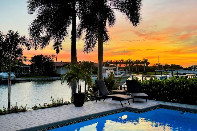 pool at dusk featuring a patio area and a water view