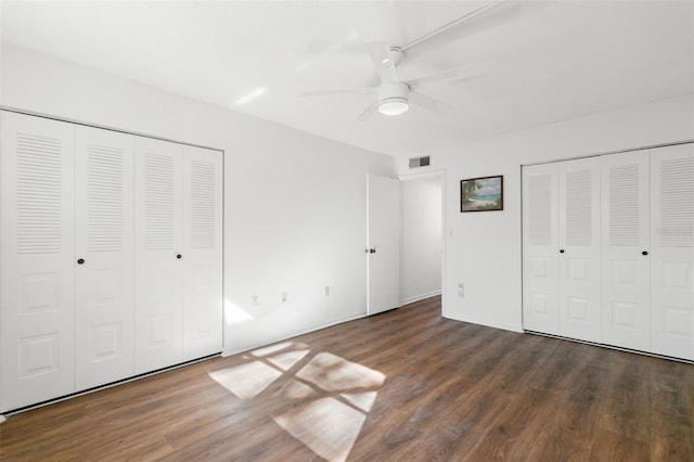 unfurnished bedroom with two closets, ceiling fan, and dark wood-type flooring