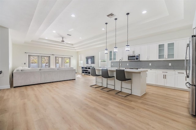 kitchen with white cabinetry, stainless steel appliances, a raised ceiling, pendant lighting, and a center island with sink