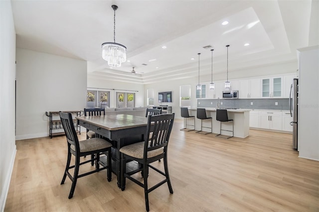 dining space featuring ceiling fan with notable chandelier, light wood-type flooring, french doors, and a tray ceiling