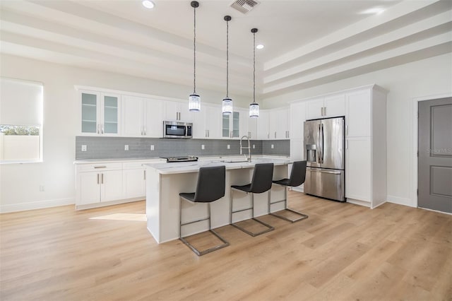 kitchen with a kitchen island with sink, white cabinetry, stainless steel appliances, and decorative light fixtures